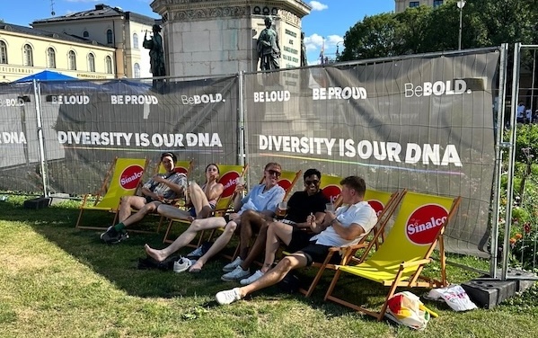 Menschen auf Liegestühlen vor den Bauzaunbannern von beBold