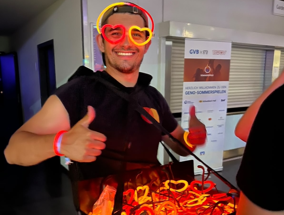 Ein Promoter trägt ein Bauchladen mit orange roten Knicklichtern, Knicklicht-Ärmbändern und Knicklicht-Brillen