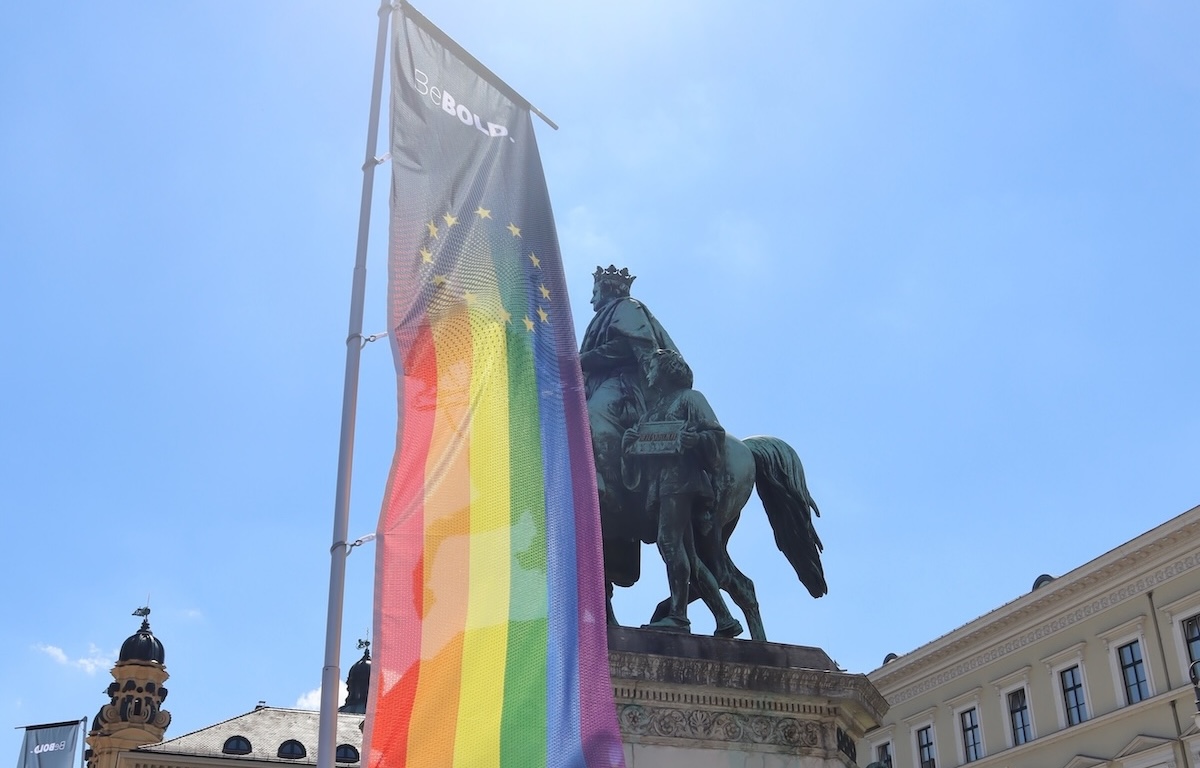 CSD München - eine Pride Fahne vor Reiter Statue und blauer Himmel