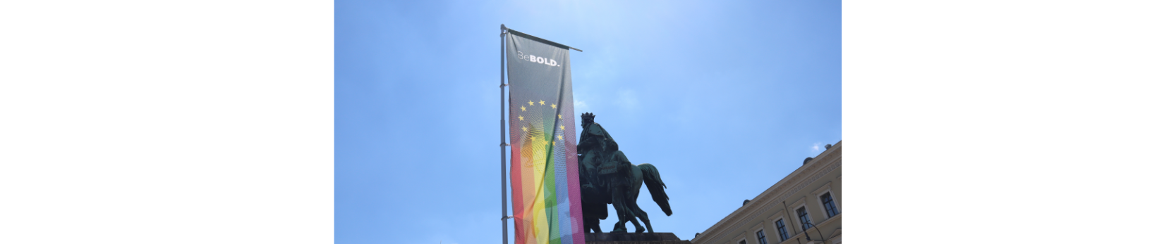 CSD München - eine Pride Fahne vor Reiter Statue und blauer Himmel