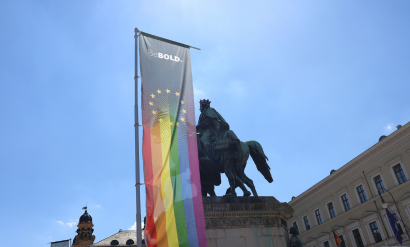 CSD München mit einer Pride Flagge vor dem Reiter Denkmal mit blauem Himmel